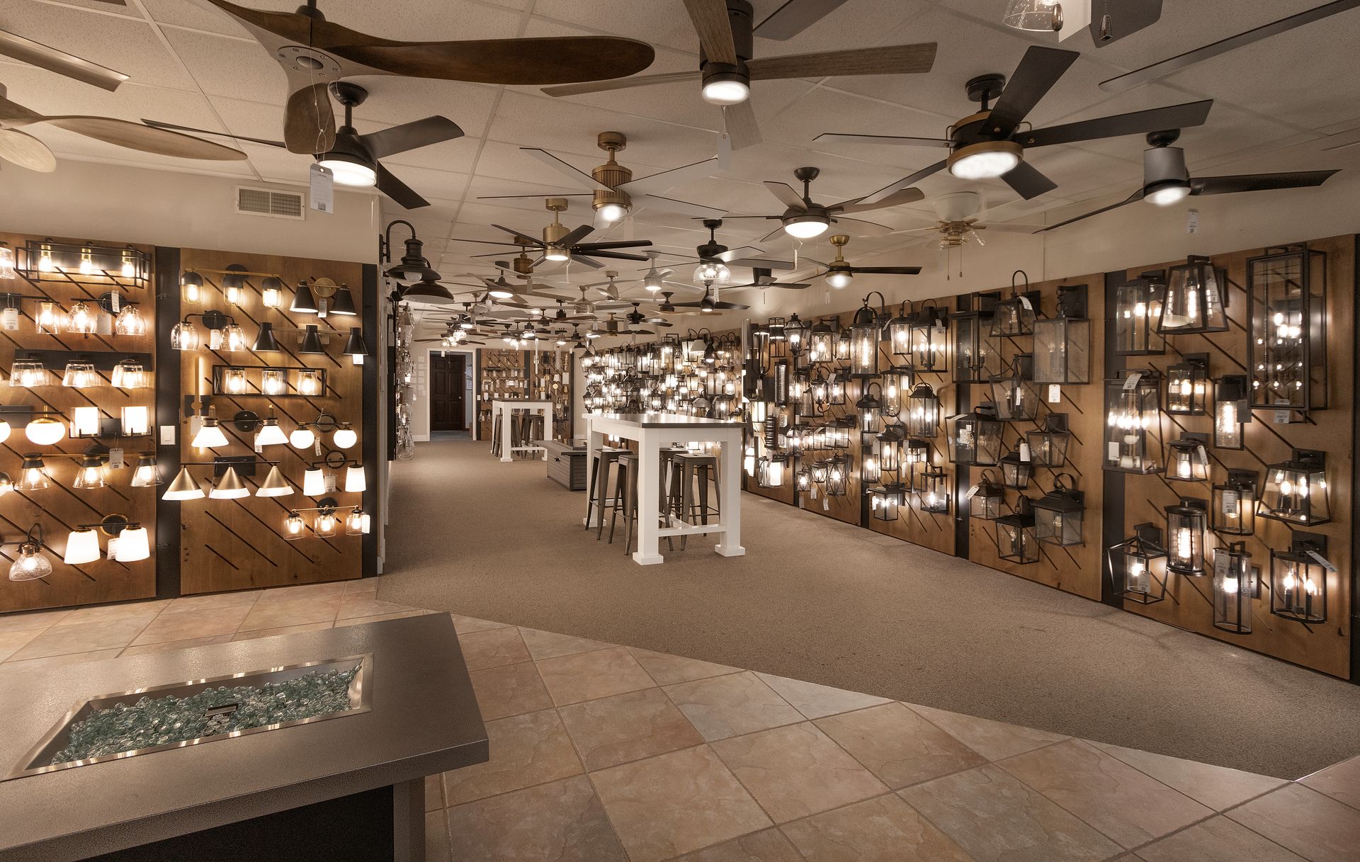 Interior of a lit retail display room with shelves of hanging lights, ceiling fans, and a central table