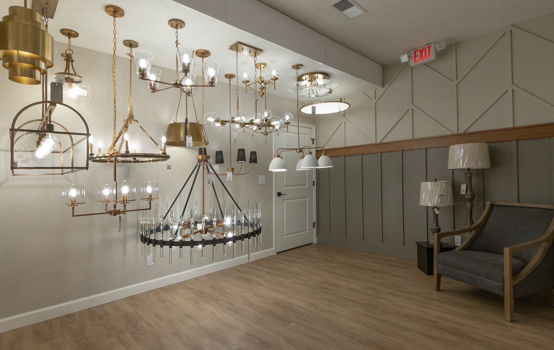 Showroom with hanging chandeliers, wood floor, gray walls, and upholstered chair near the corner.