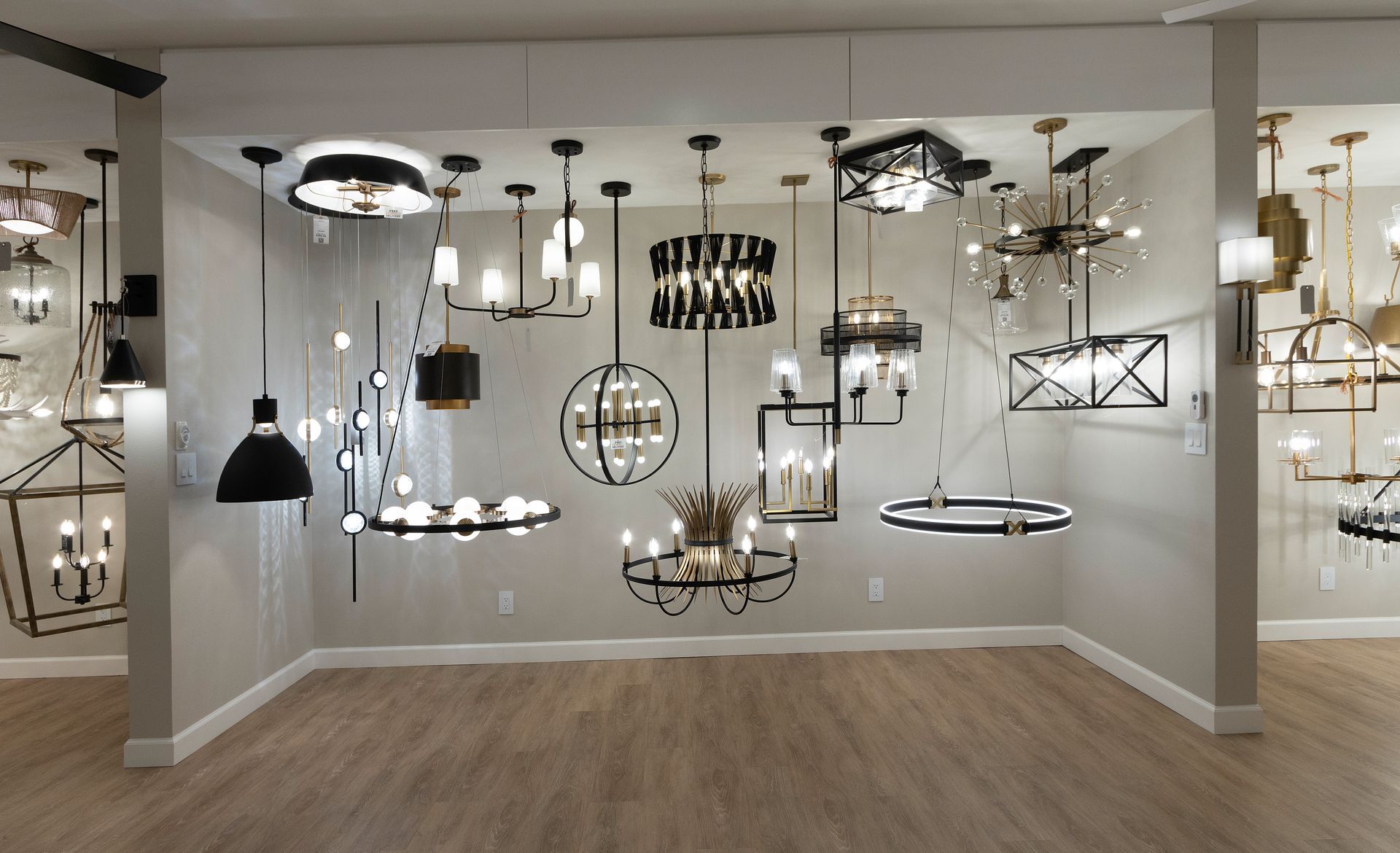 Display room with many hanging light fixtures and chandeliers on white walls and wood floor