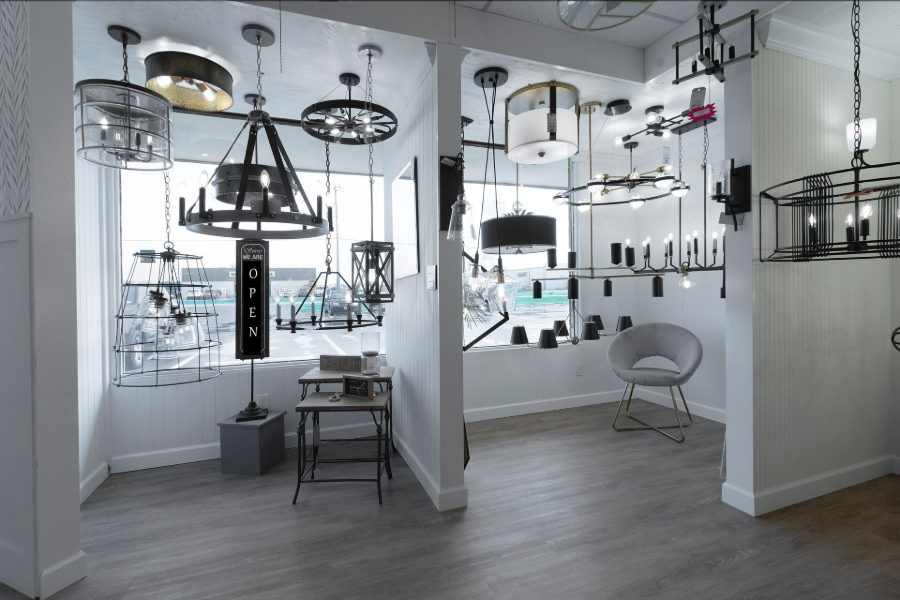 Bright showroom with hanging pendant lights, chandeliers, and modern seating in a white interior.