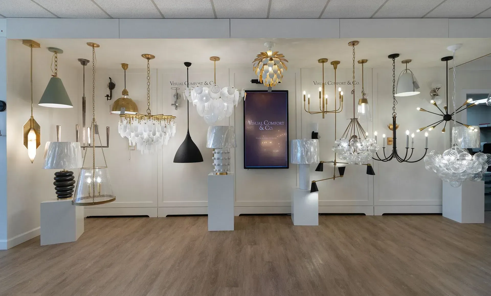 Modern showroom displaying assorted hanging chandeliers and pendant lights on white pedestals