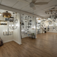Lighting showroom with many hanging chandeliers and pendant lights in a spacious room with wood flooring