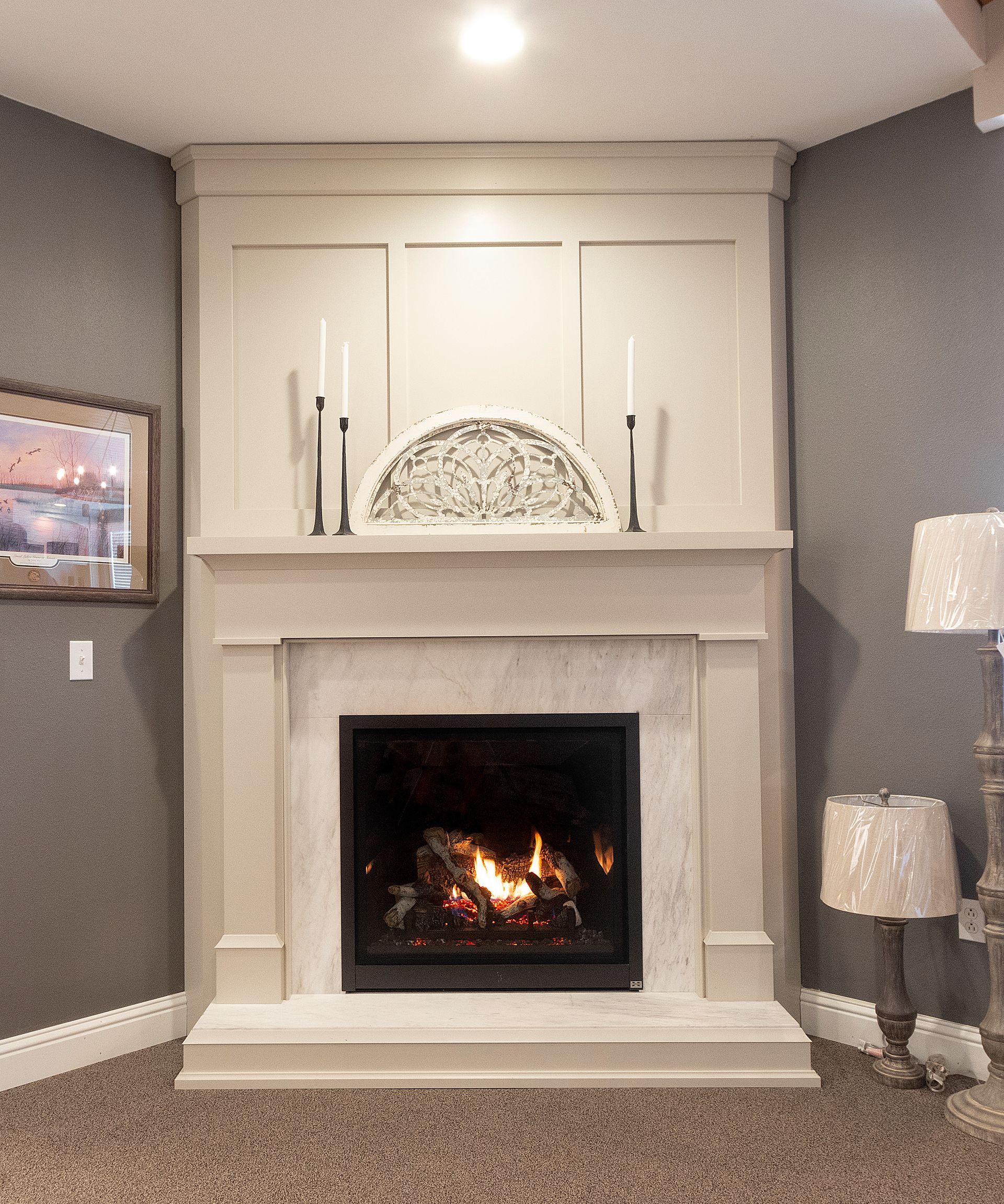 Modern white fireplace with lit fire, built-in cabinets, and gray walls in a living room
