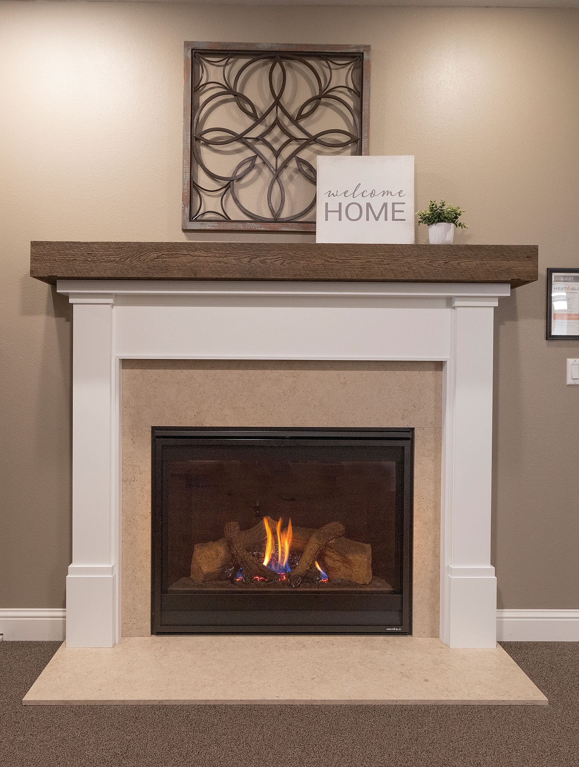 White fireplace with a burning fire, stone mantel, and decorative home sign in a living room.