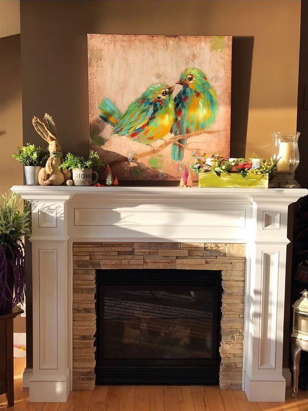 Fireplace mantel with colorful bird painting, plants, and decorative accents in a cozy living room