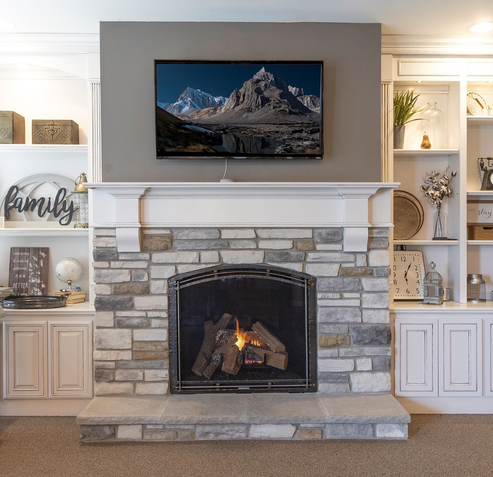 Stone fireplace with lit fire, mounted TV above, and white built-in shelves in a living room.