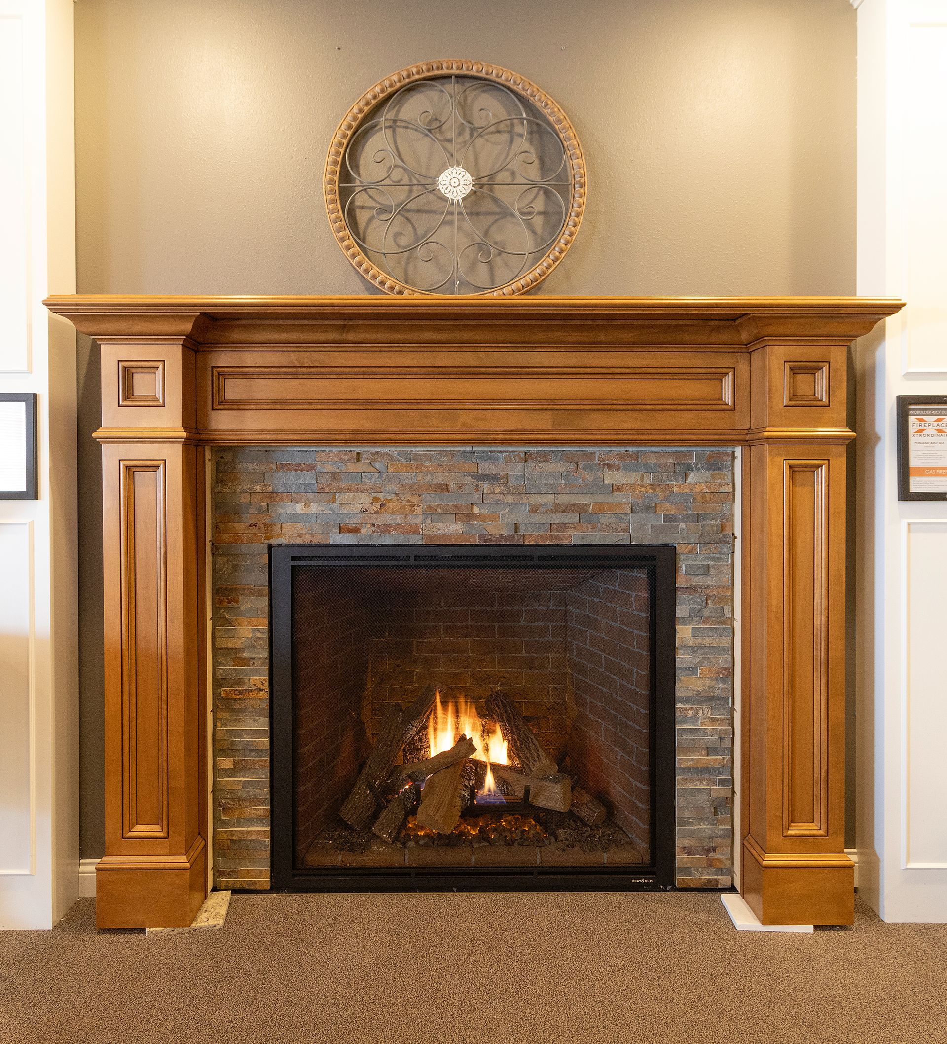 Wooden fireplace mantel with stone surround and a lit fire in a carpeted room