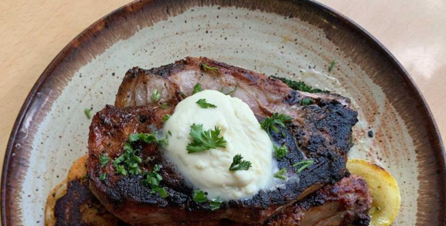 Grilled steak topped with herb butter on a rustic ceramic plate