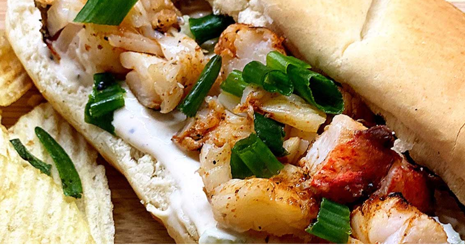 Close-up of a grilled hot dog topped with chopped onions, bacon, and green onions in a bun
