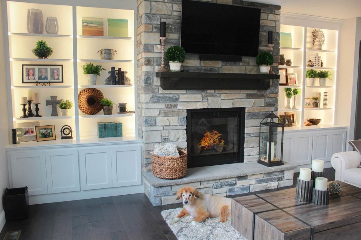 Cozy living room with built-in shelves, stone fireplace, and a small dog on a rug