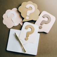 Question marks on paper cards above an open notebook on a dark background