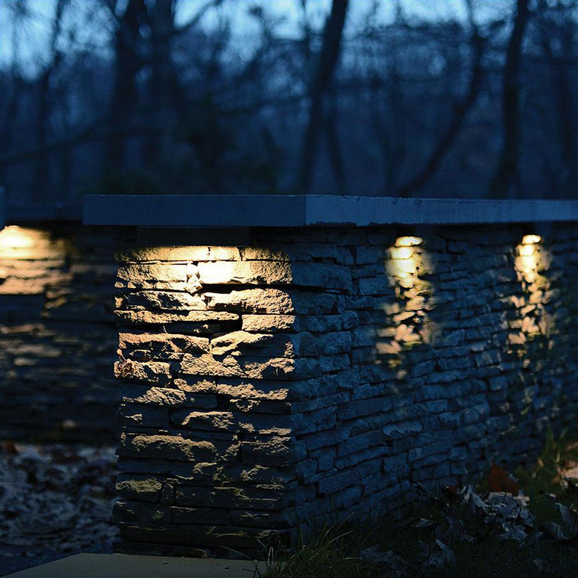 Stone wall with warm lights glowing in a dark wooded outdoor scene at dusk