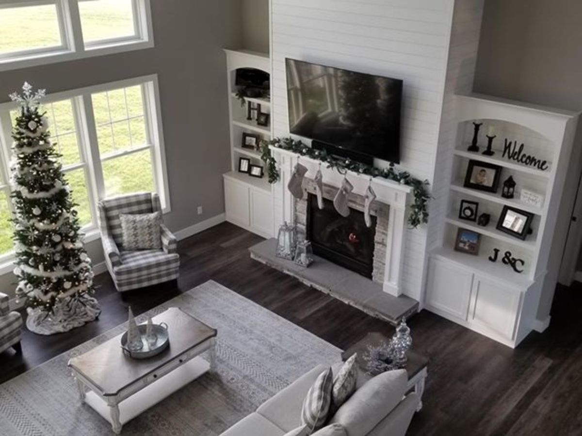 Bright living room with a decorated Christmas tree, fireplace, TV, and white shelves on dark wood floors