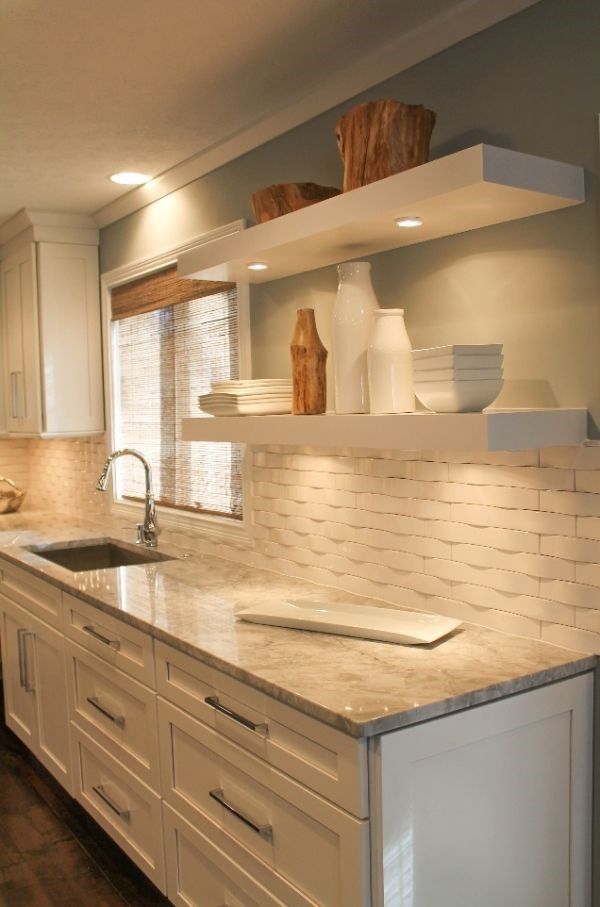 Modern kitchen with marble countertop, white cabinets, floating shelves, and tiled backsplash by a window.