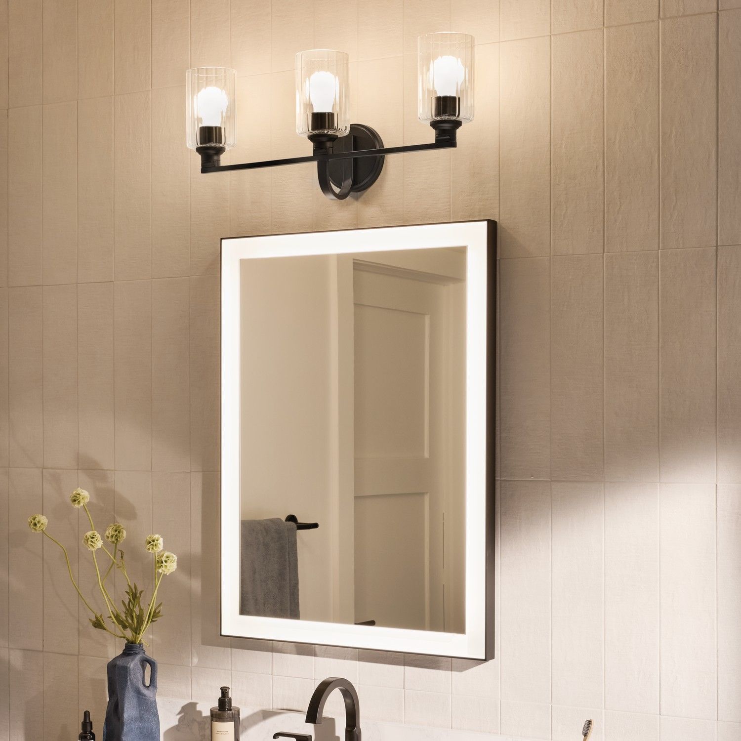 Bathroom vanity with a white-framed mirror, black three-light sconce, and beige tiled wall