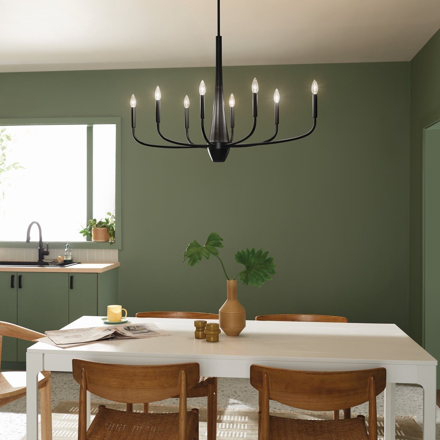 Modern dining room with green walls, white table, wooden chairs, and black chandelier.