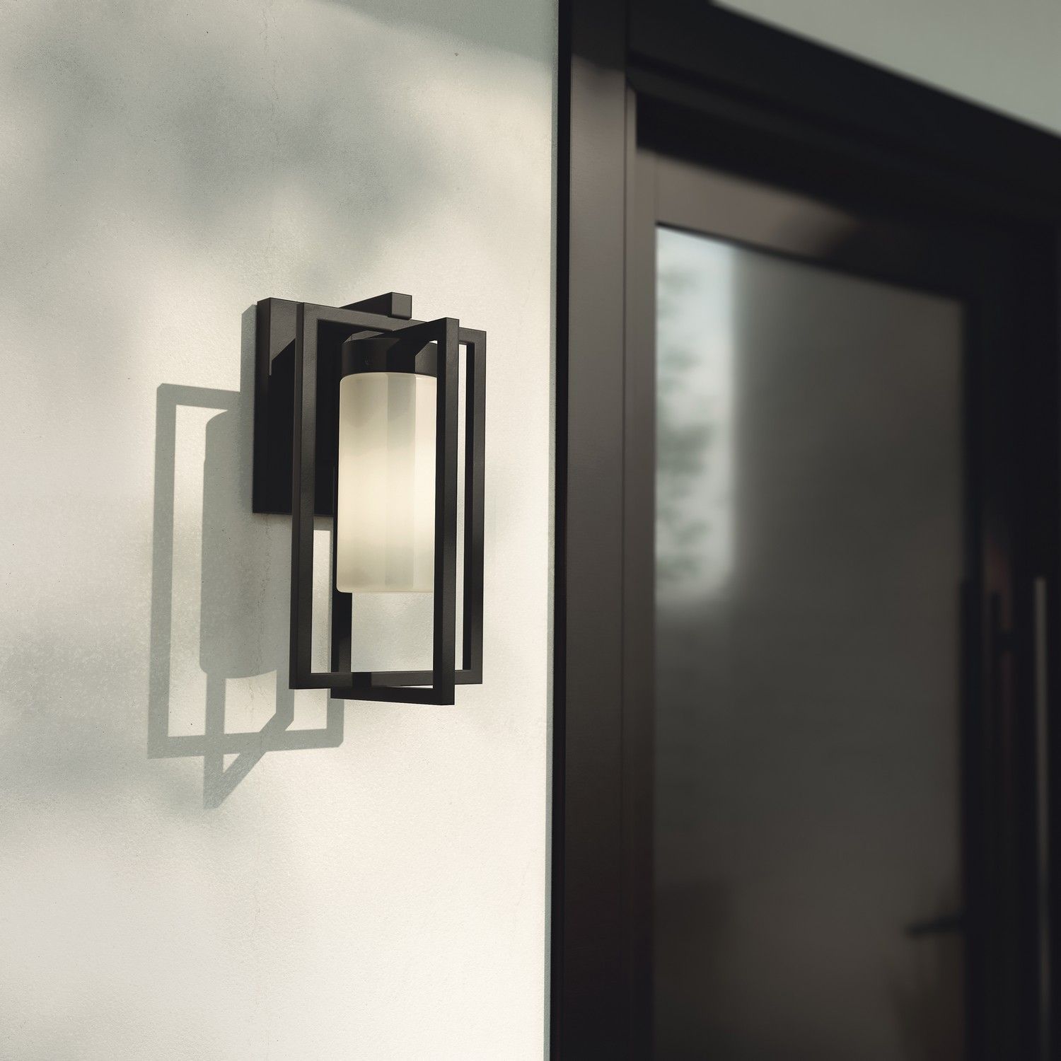 Black wall sconce on a white exterior wall beside a dark doorway, casting a geometric shadow