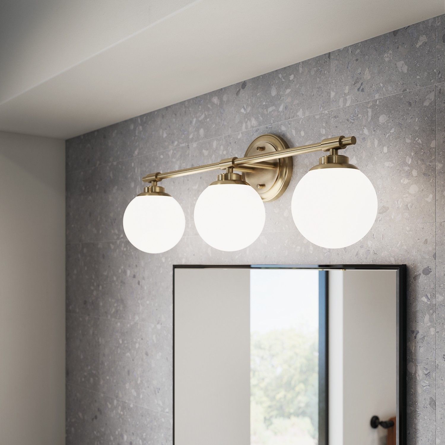Brass vanity light with three frosted globe bulbs above a bathroom mirror on a gray textured wall