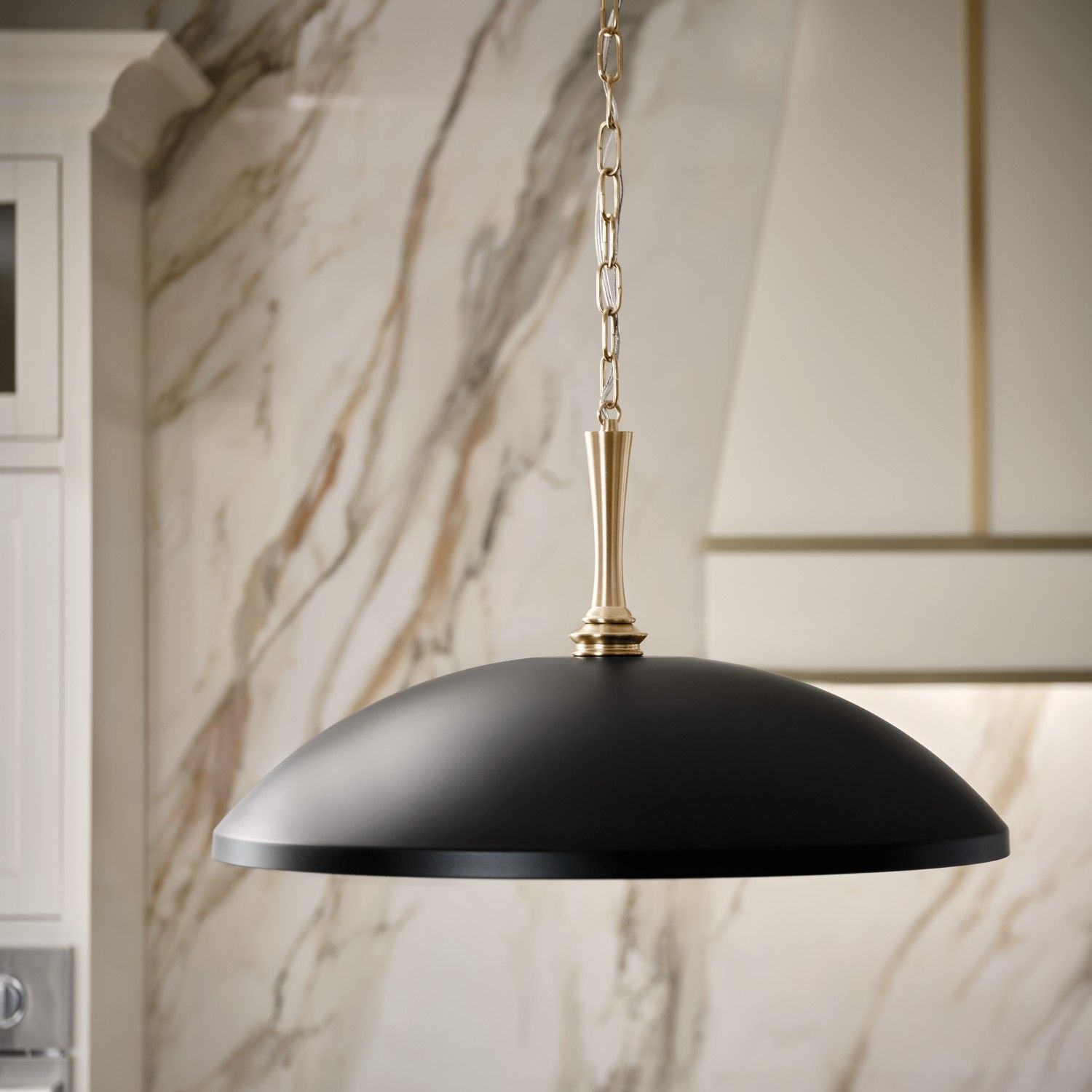 Black dome pendant light with gold chain hanging in a marble-accented interior
