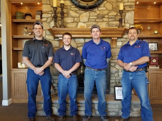 Four men in blue shirts stand behind a wooden counter in a rustic lodge-style room