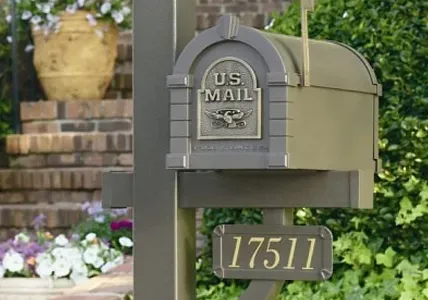 Black wall-mounted mailbox labeled “POST” on a stone wall beside green ivy and red flowers