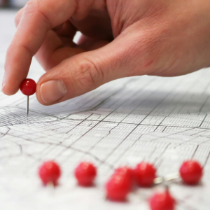 Hand placing a red pushpin on a map with several red pins nearby