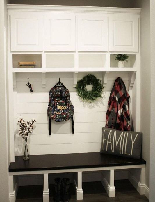 White entryway bench with cubbies, hooks, wreath, backpack, coat, and FAMILY sign