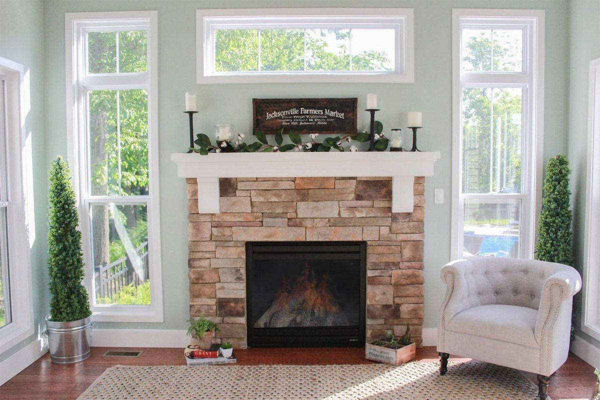 Bright living room with a stone fireplace, white mantel, tall windows, and a light armchair
