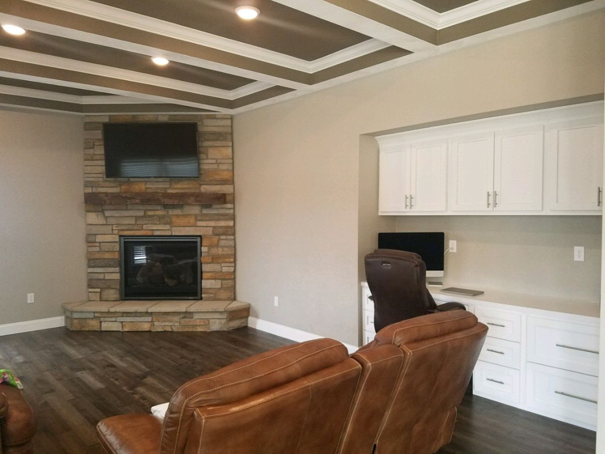 Living room with stone fireplace, wall-mounted TV, and built-in desk beside brown leather chairs.