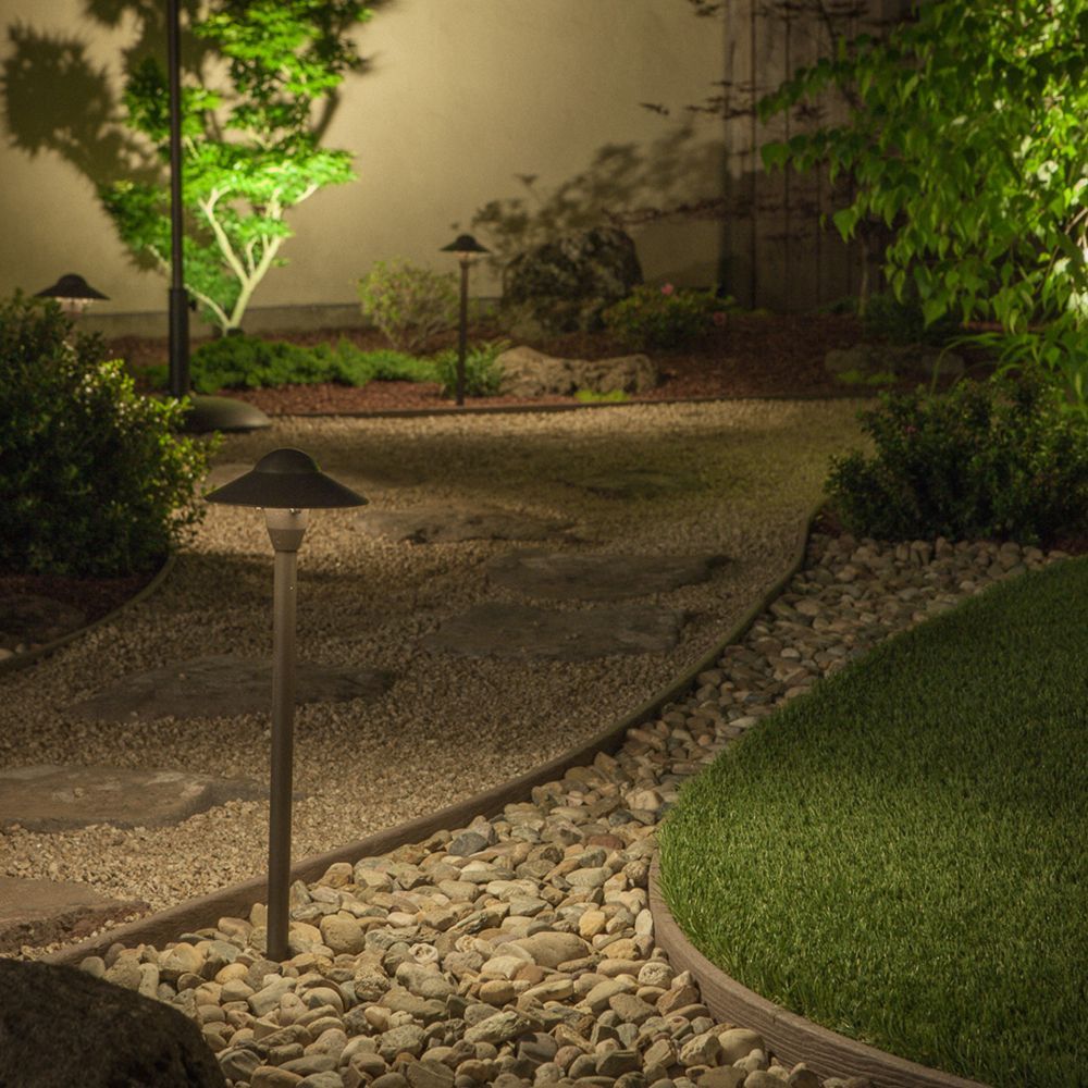 Landscaped garden path at night with gravel, grass, and soft lighting.