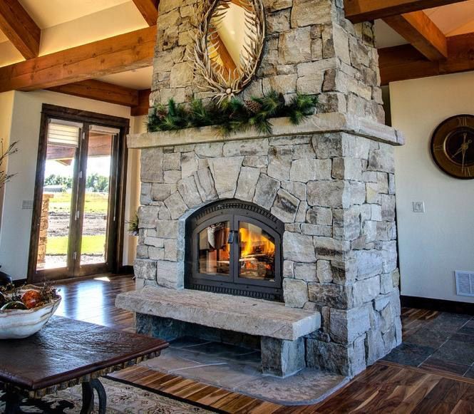 Cozy living room with a stone fireplace, wooden beams, and large windows overlooking the outdoors