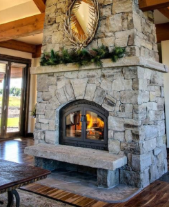 Cozy living room with a stone fireplace, wooden beams, and large windows overlooking the outdoors