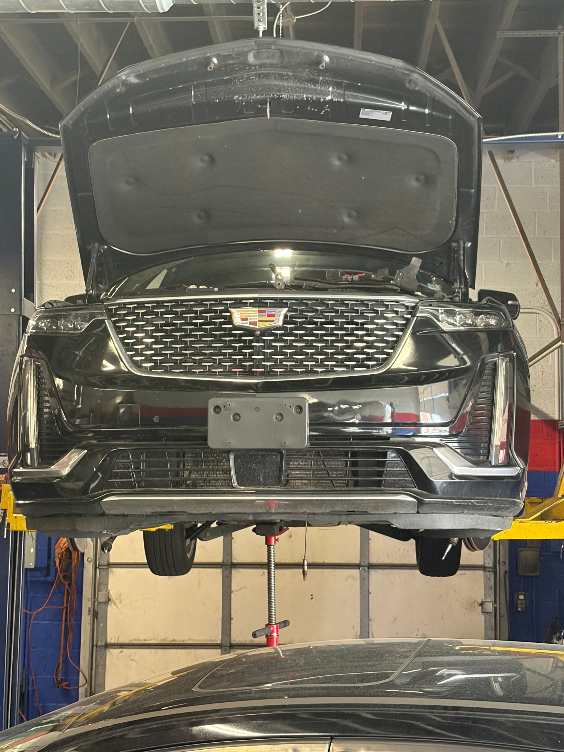 Black Cadillac SUV on a lift with hood open in an auto repair shop