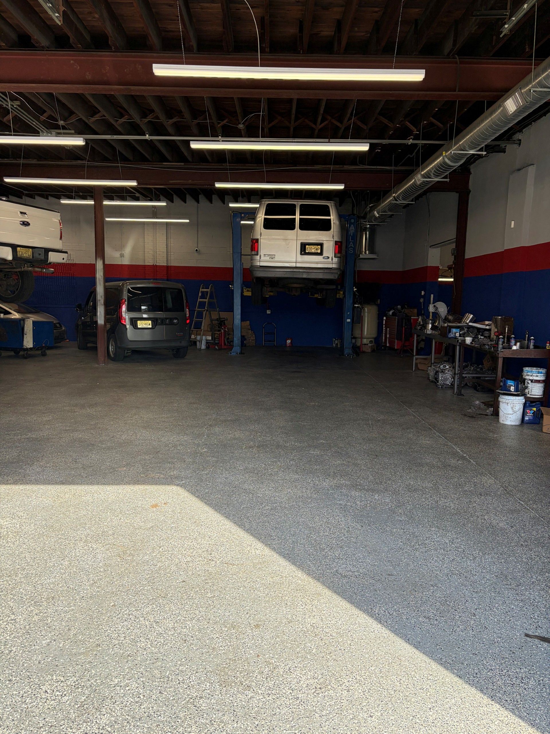 Auto repair garage with cars on lifts, tools, and bright sunlight on the floor