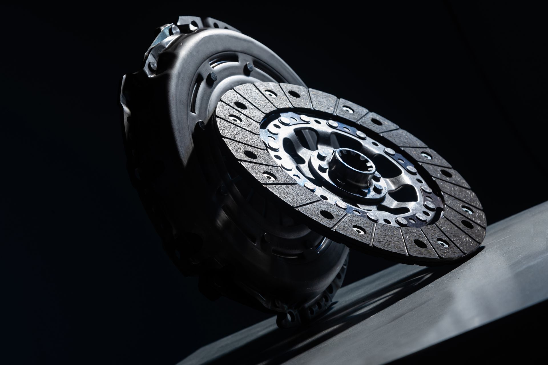 Close-up of a silver car brake rotor and caliper in a dark garage, lit dramatically from above