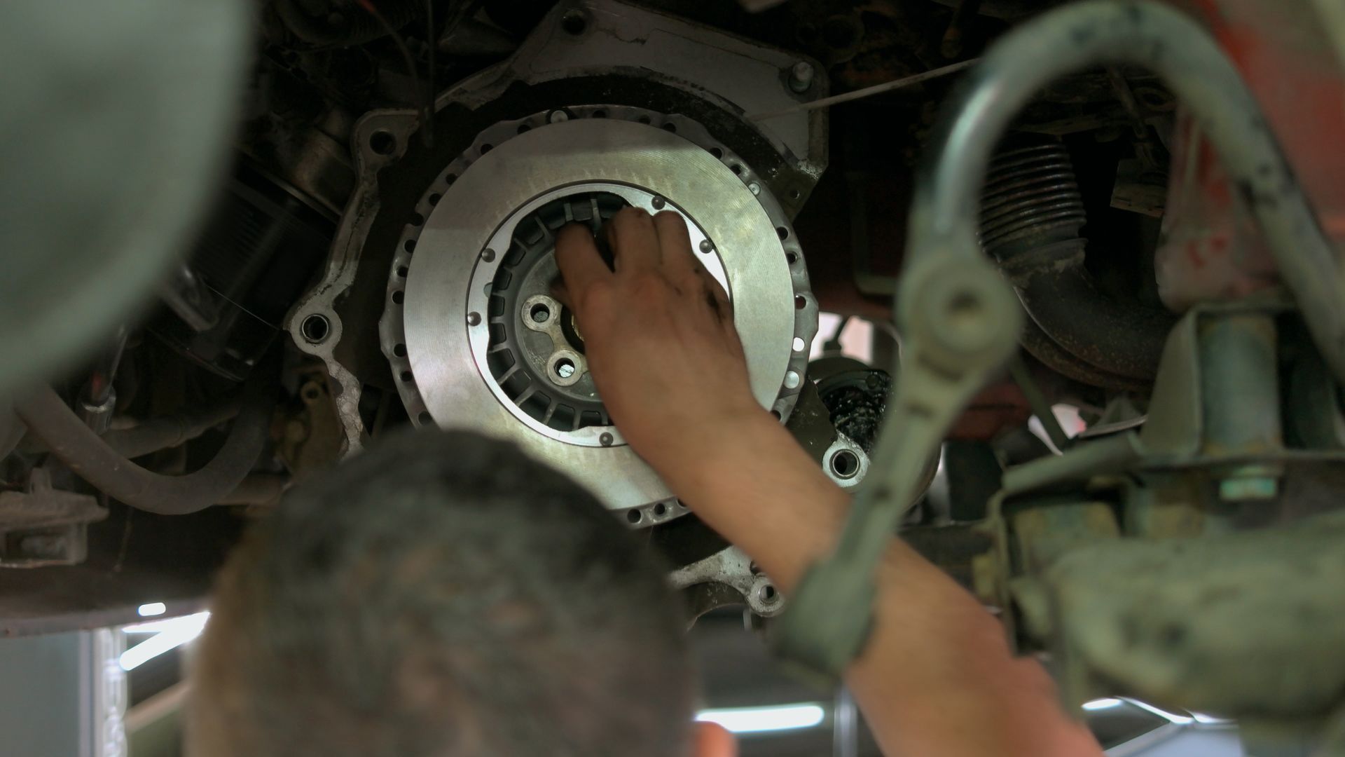Hands working inside a circular metal engine or machine component with hoses and wiring nearby.