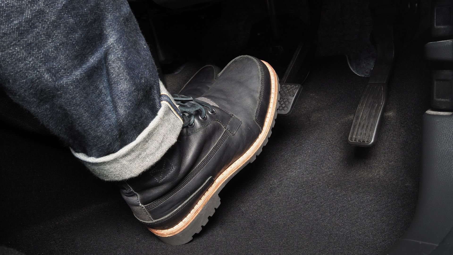 Person’s foot in a black sneaker and jeans resting on a car floor mat with a seat belt strap nearby