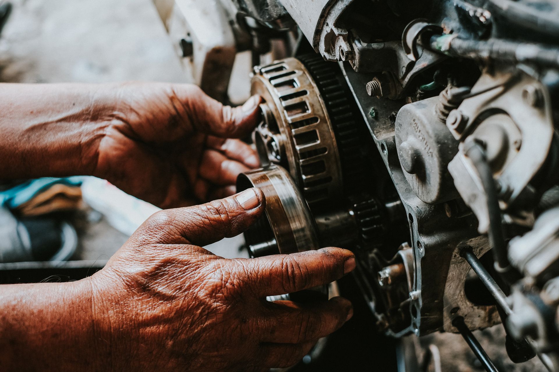 Hands working on a car engine, holding a metal gear in a greasy mechanical repair scene