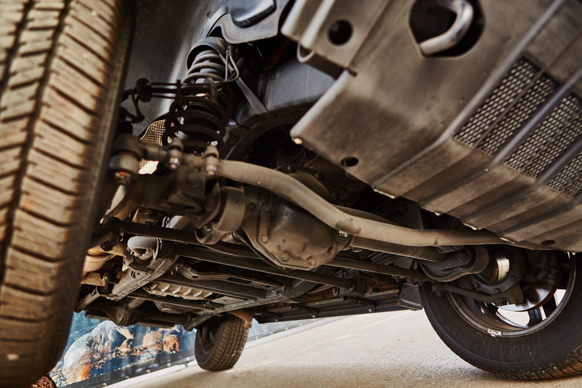 Undercarriage of a car on a lift, showing suspension, exhaust, and front wheel from below