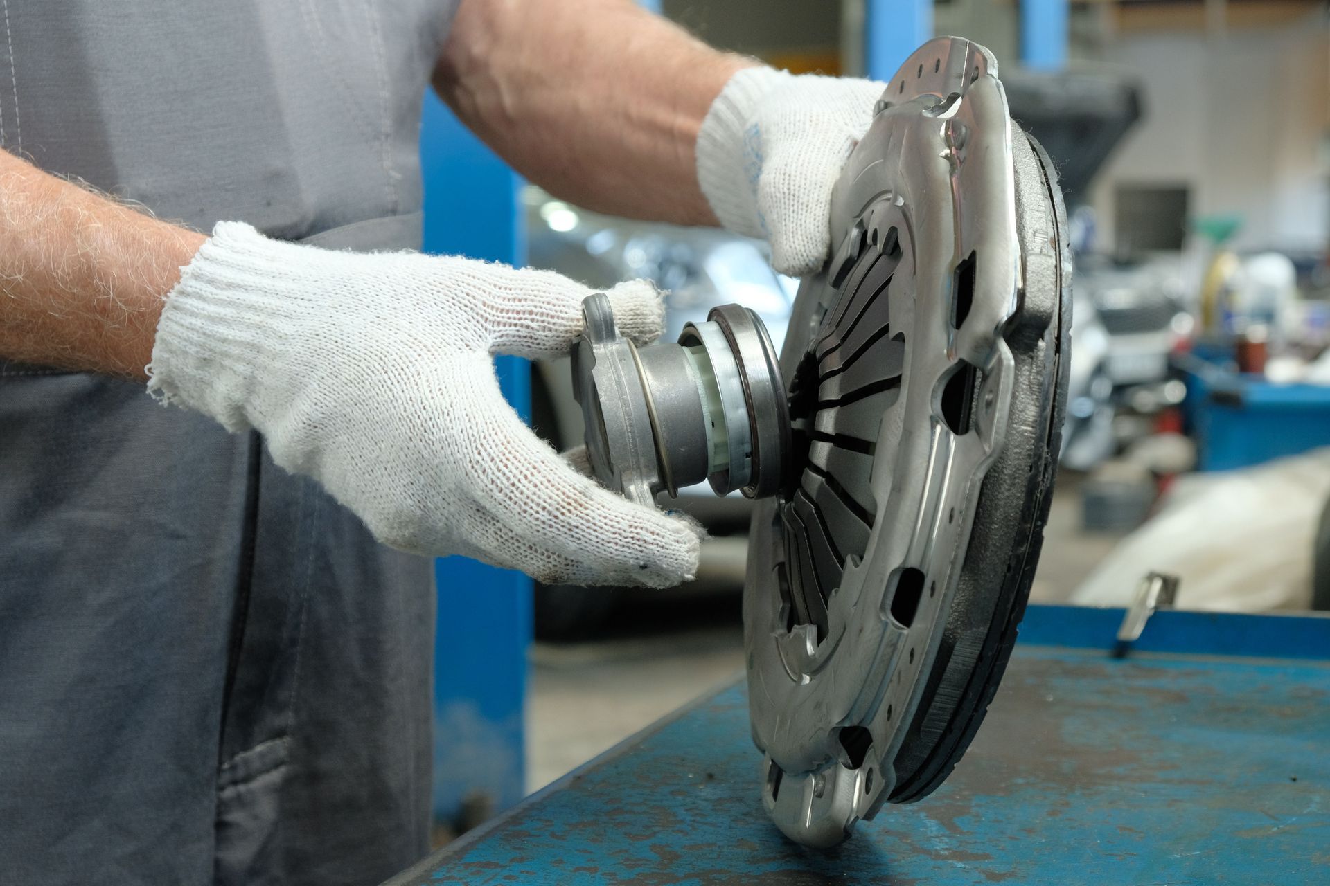 Gloved hands installing a metal car clutch assembly on a workbench