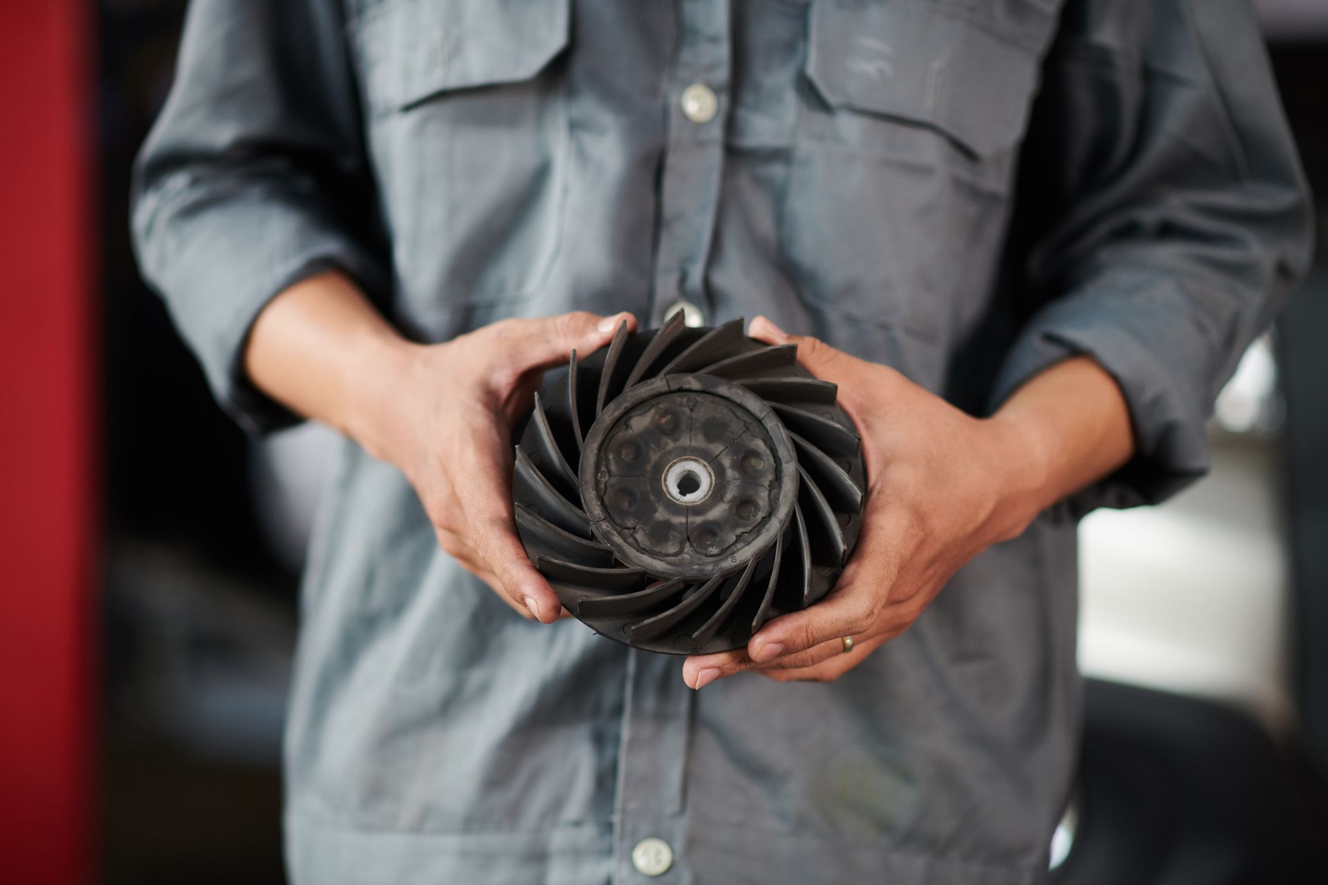 Hands holding a black turbo fan rotor against a gray shirt background