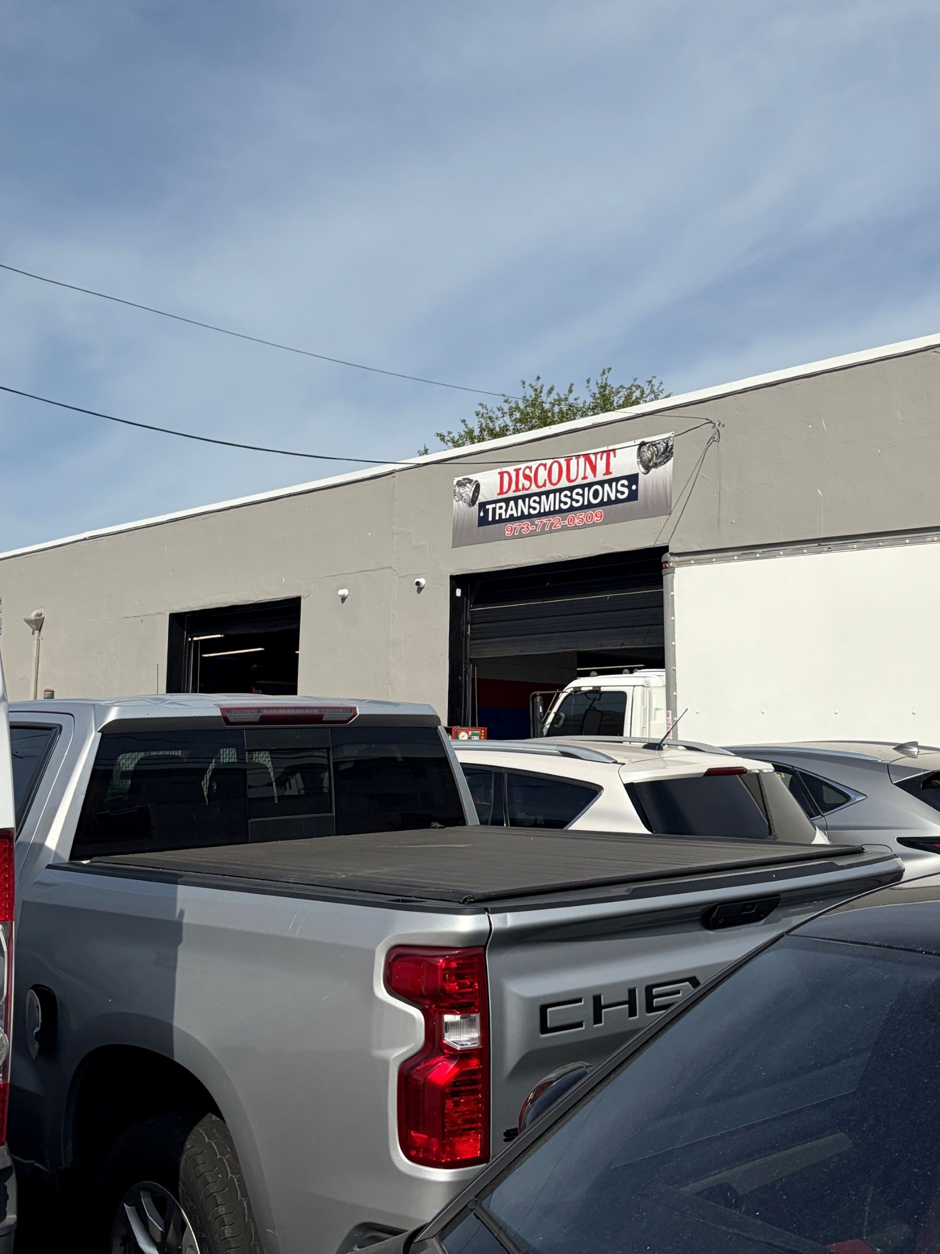 Truck parked outside a warehouse with a red-and-white sign above the entrance.