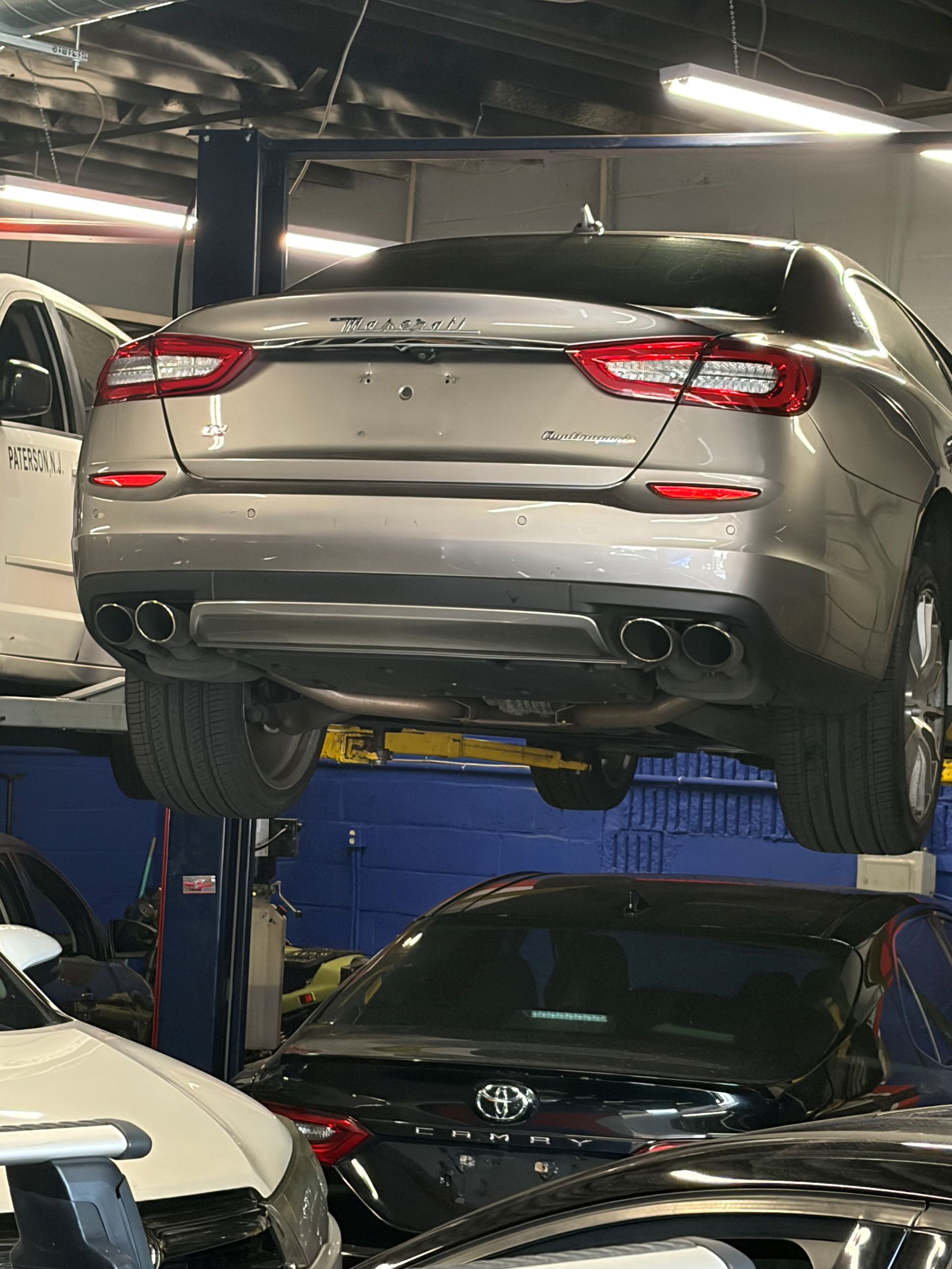 Silver SUV lifted on a car hoist in a garage, with another car parked below.