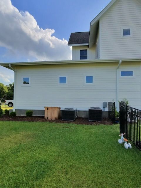 White house exterior with small fenced lawn, AC units, and a partly cloudy sky