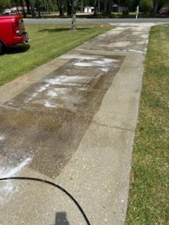 Residential sidewalk with a large wet patch and white residue, beside grass and a parked red truck