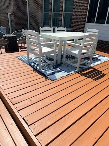 White patio table and chairs on a wooden deck with a blue patterned rug near a brick house