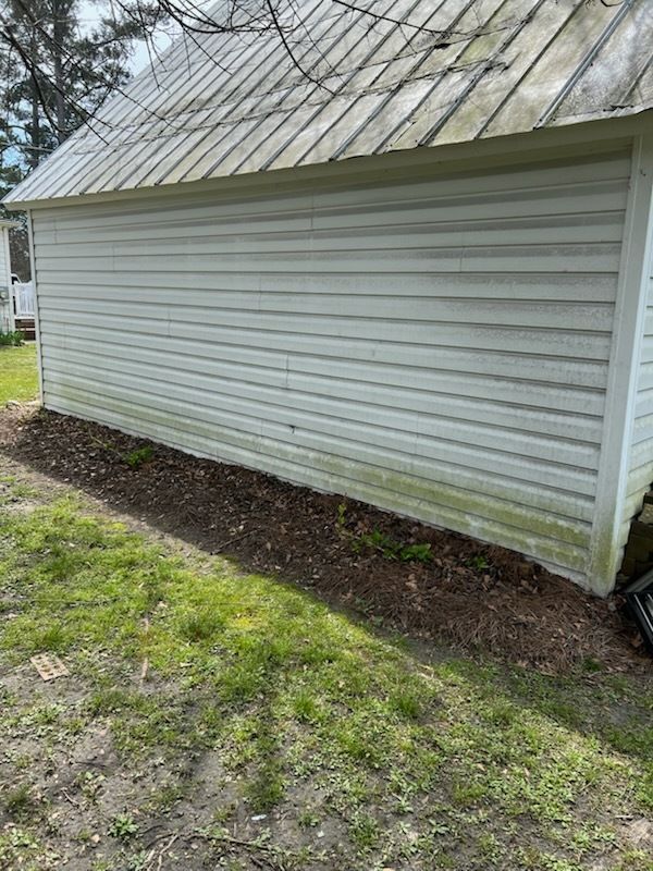 White-sided shed with a metal roof and a dirt strip along the foundation in a grassy yard
