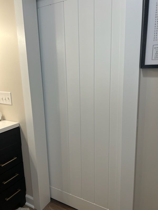 White vertical slatted closet door beside a dark vanity in a bathroom corner