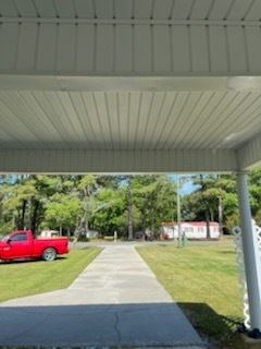 Covered walkway with a sidewalk, red pickup truck, green lawn, and trees leading to a white building.