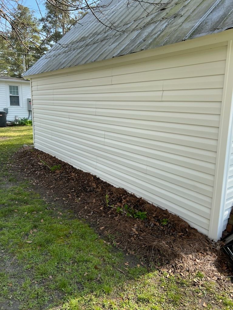 White house siding and metal roof beside a grassy yard and mulched foundation edge